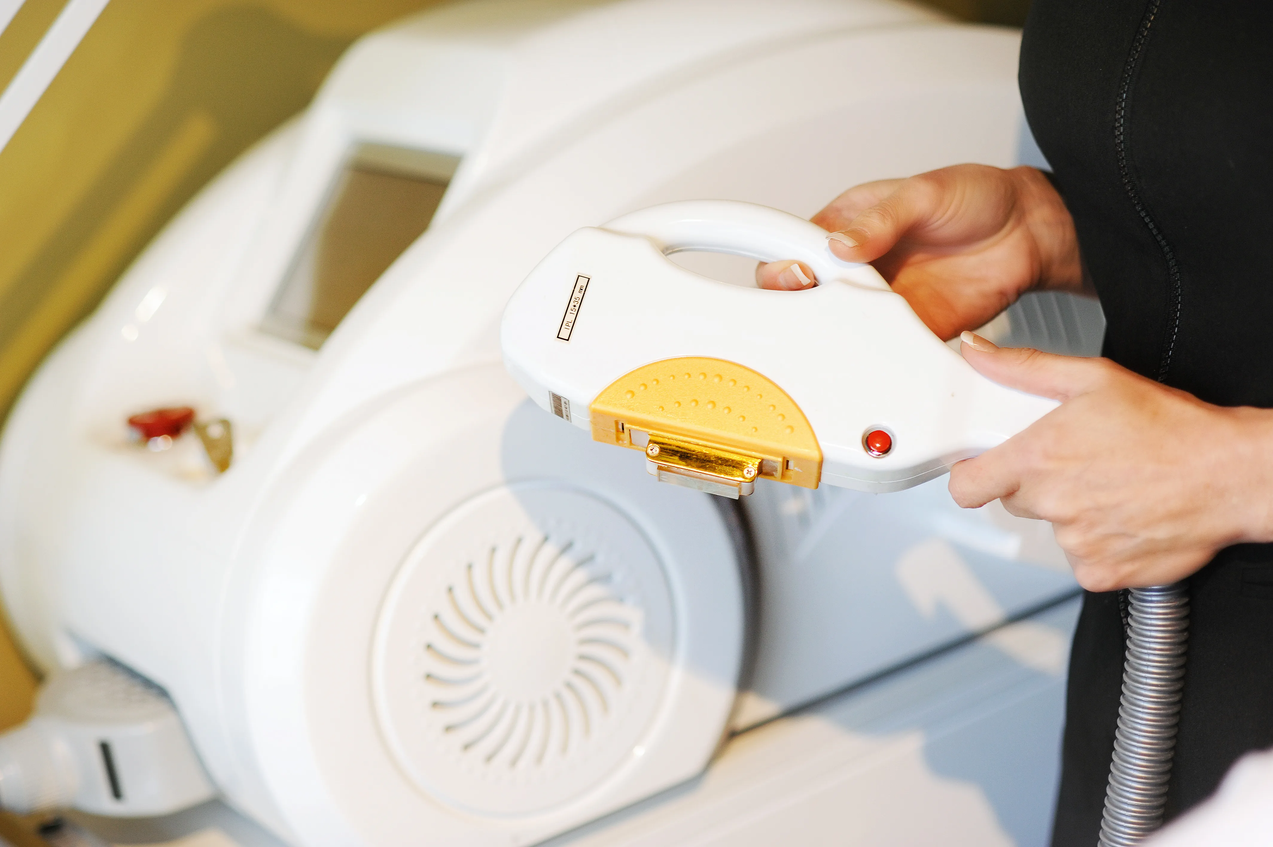 Hands guiding an IPL laser handpiece over treatment equipment at Envisage Beauty